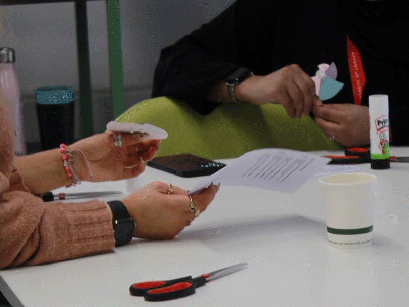 Close up of the hands of two people assembling rose badges as part of International Women's Day visualization activities