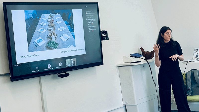 Damla Çay from Moholy-Nagy University of Art and Design, Budapest speaking in the Diverse CDT data vis lab and showing a photograph of a meal laid out with data ceramics, specially designed to represent ecological disruption in areas round Lake Balaton in Hungary.