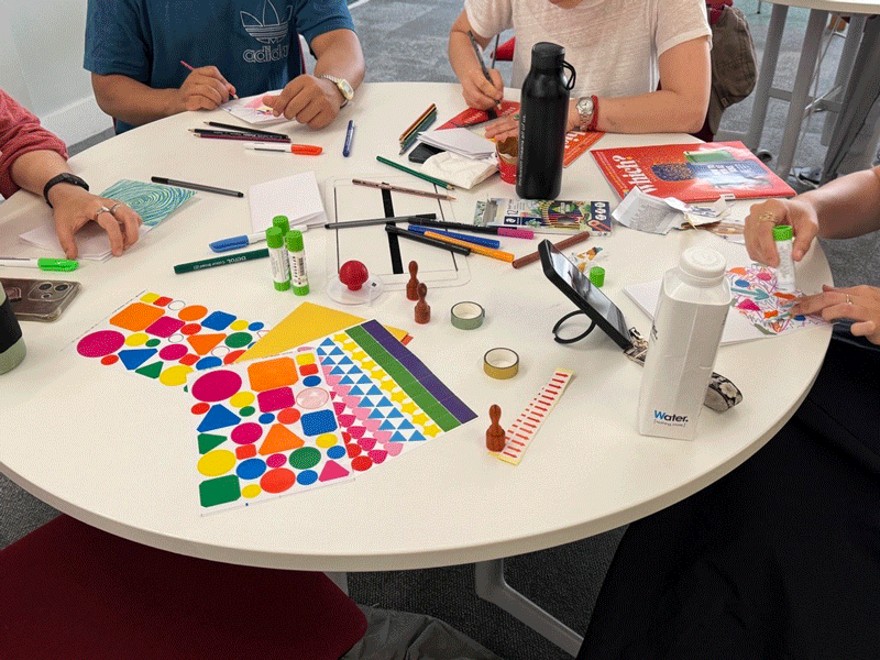 A circular white table with brightly coloured shapes, scissors and glue to represent the creative process during the Fold, Encode, Reflect session as part of London Data Week.